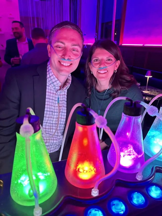 Two smiling guests at a vivid purple-lit evening event